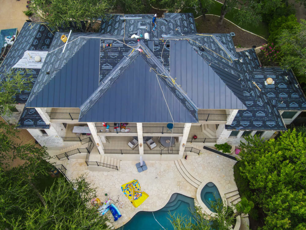 A Texas Roof Repair crew on the roof of a large home in Texas installing a new metal roof.